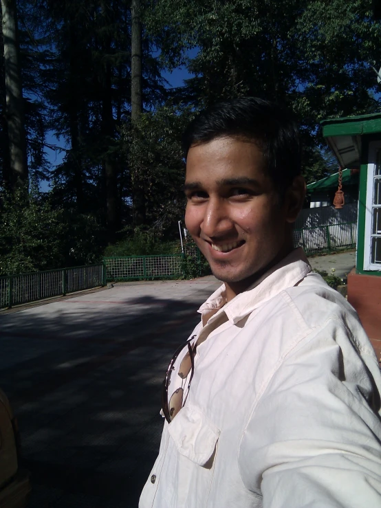 a smiling man standing by a house, with trees and buildings