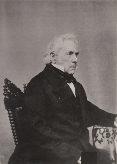 an old pograph of an older man in a suit sitting