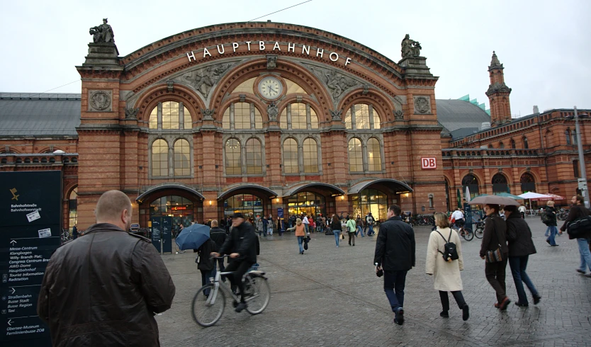 people are walking and riding bikes in front of a train station