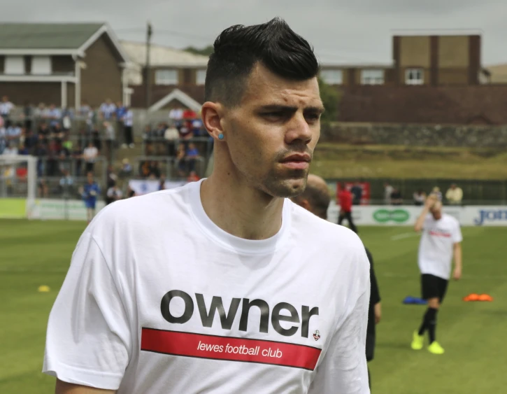 man with earrings wearing a owner shirt and standing near others playing frisbee