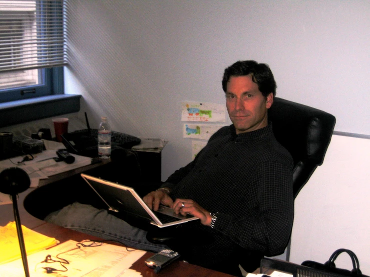 a man in black sweater sitting at desk on laptop