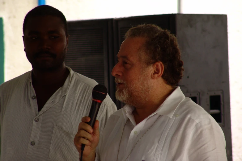 a man in white is holding a microphone and a male wearing black looks on