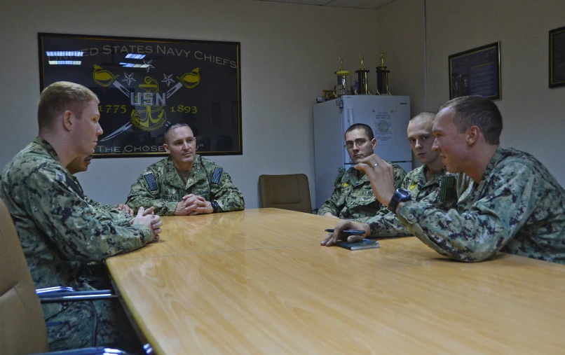 four men in army uniforms are sitting around a long table