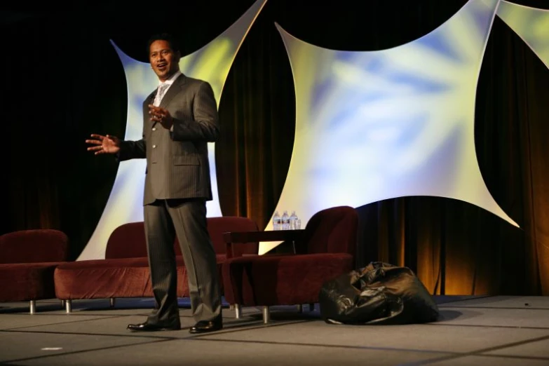 man speaking at an event wearing a gray suit