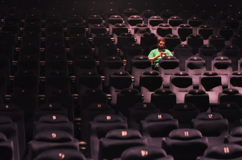 a man in green shirt sitting behind a row of empty seats