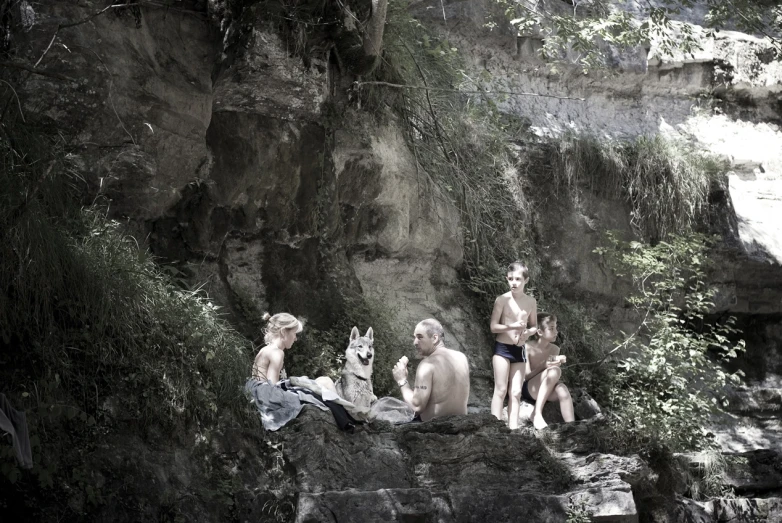 three people on a rocky ledge next to some trees and grass