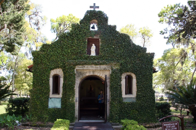 a small church covered in greenery and a cross on top