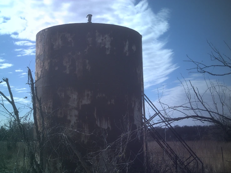 an old rusted water tank sits near a field with weeds