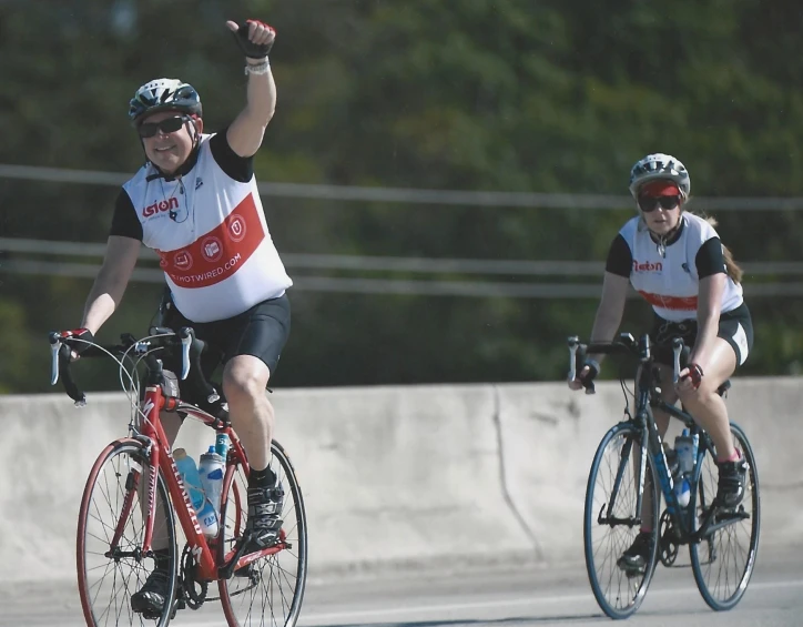 two bicyclists giving thumbs up and the other one riding