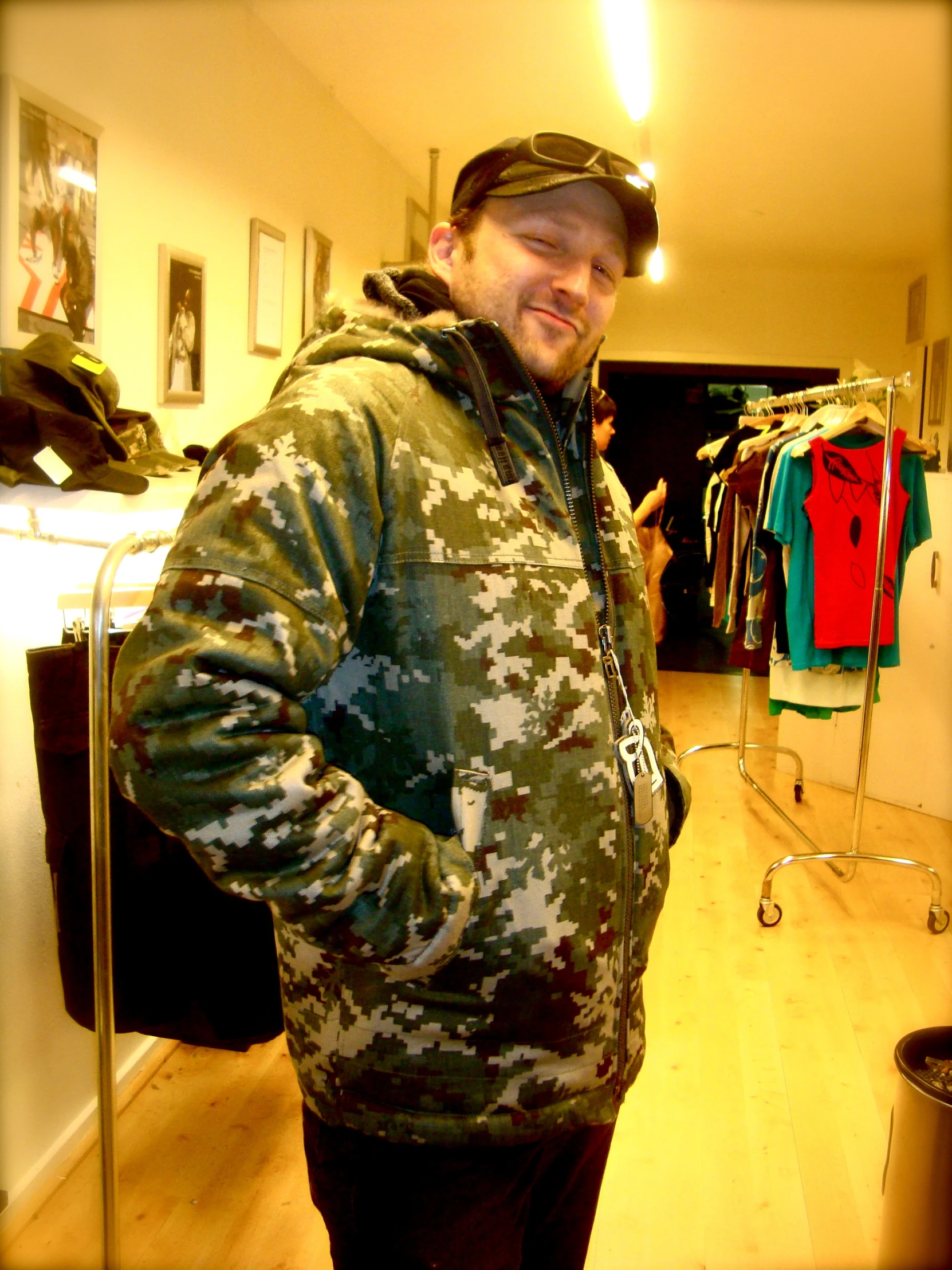 man wearing camouflage jacket in clothing store looking into camera
