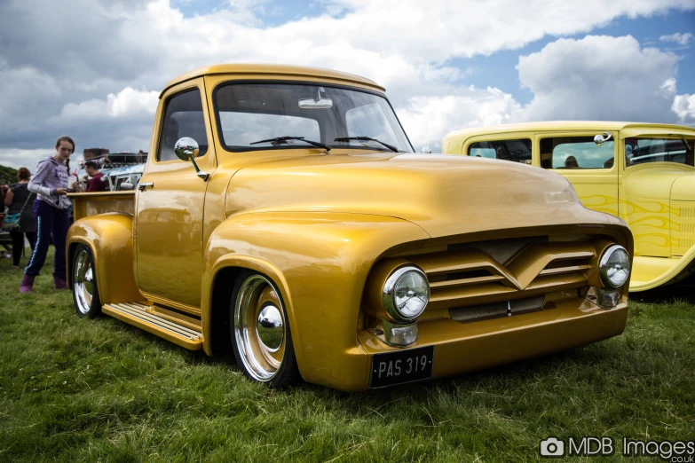 vintage yellow truck parked in grassy area near woman