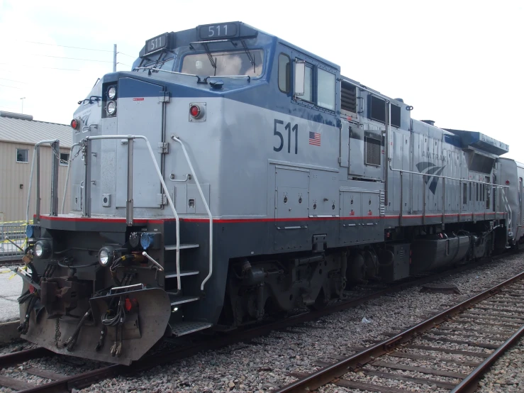 a grey train traveling down train tracks next to a tall building