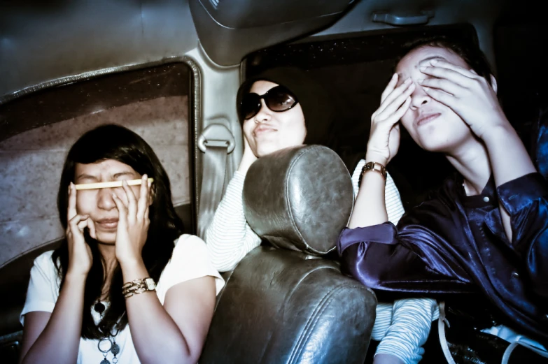 three women in the back seat of a car look surprised as they are being pographed through binoculars