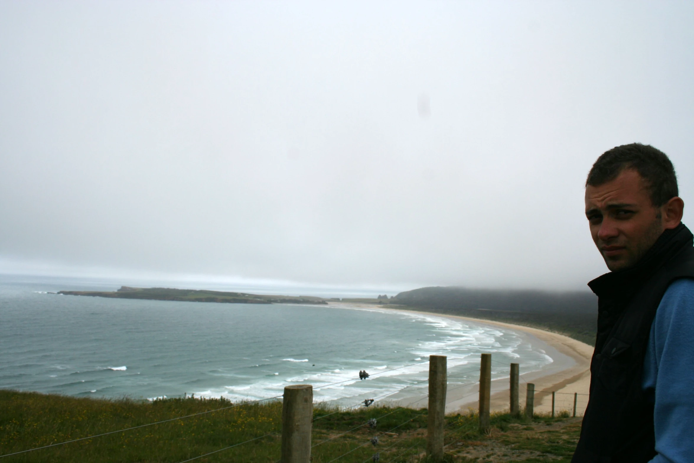 a man standing in front of the ocean with the view to a beach