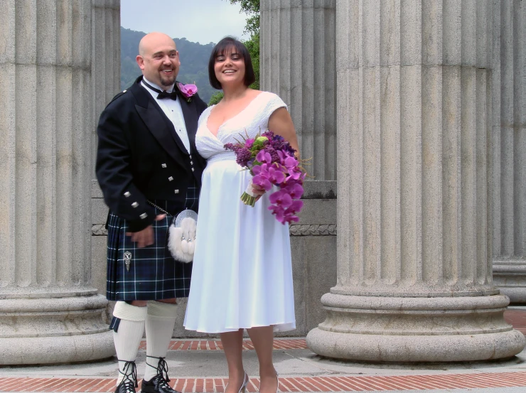 a woman and man in white dresses standing beside some columns