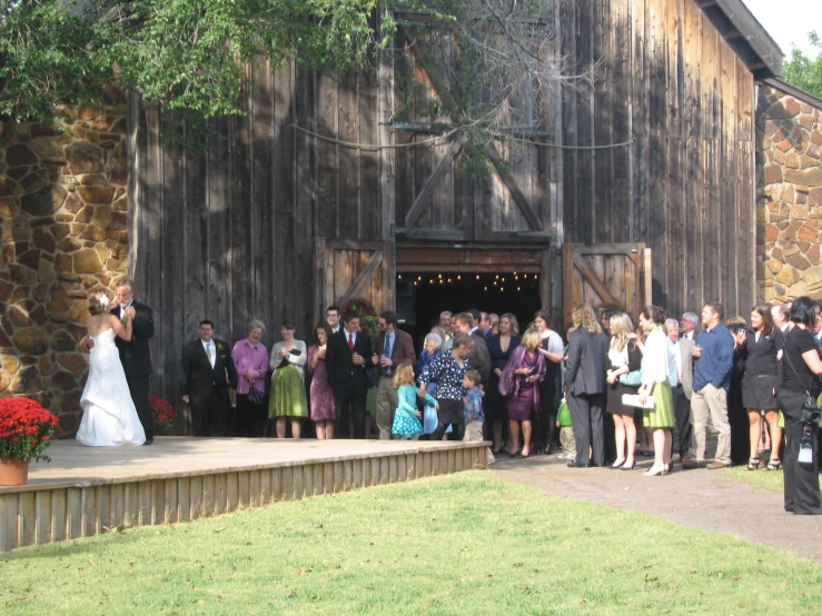 many people are outside near a rustic barn