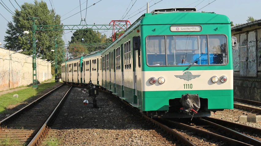 a green and white train next to a building on tracks