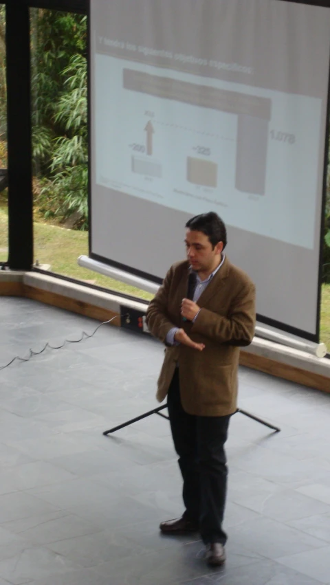 man in suit speaking on stage with screen behind him