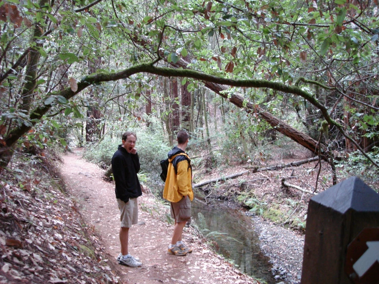 two men standing on a trail next to a stream