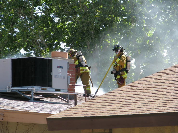 two fire fighters on top of a house next to an air conditioner