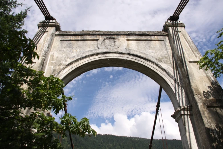 a large stone arch with a sky and trees in front