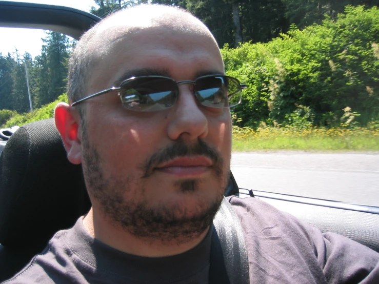 man in sunglasses with a mohawk drives in a car