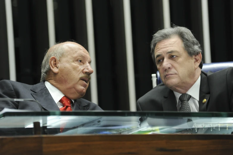 two men are sitting in suits talking to each other