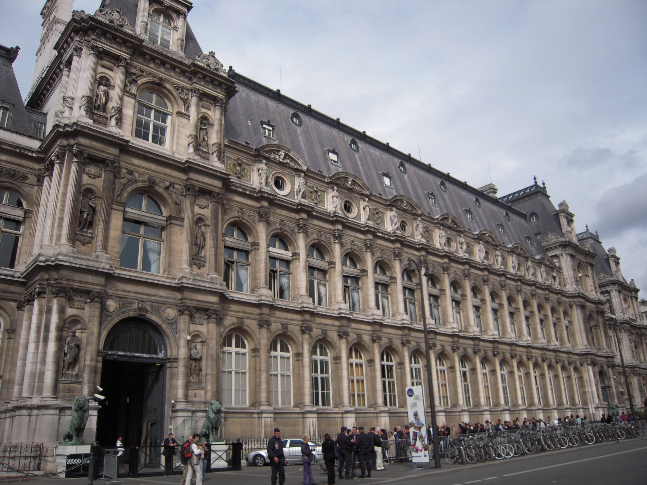 people stand outside of an ornate building with bikes parked in front of it