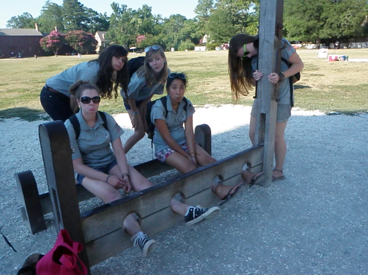 group of girls sitting on a wooden bench with one another near by