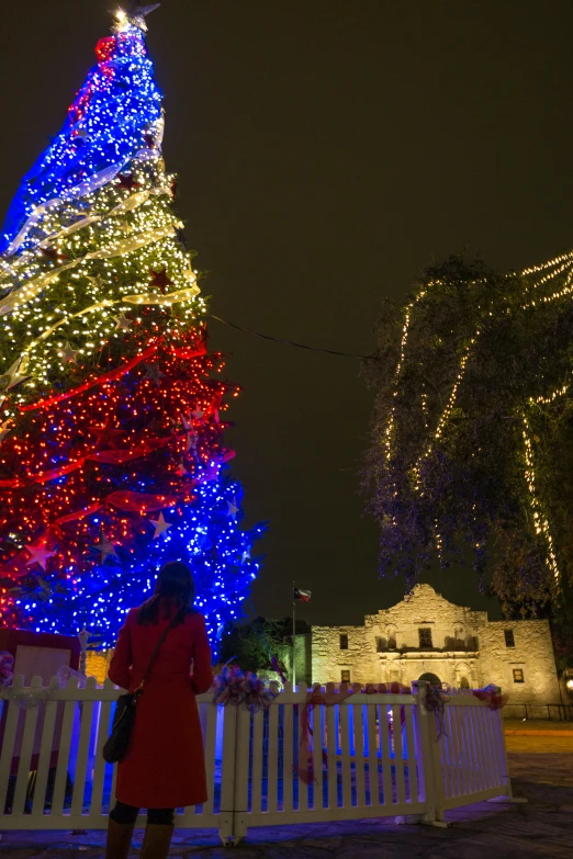 a woman in red dress standing near a christmas tree