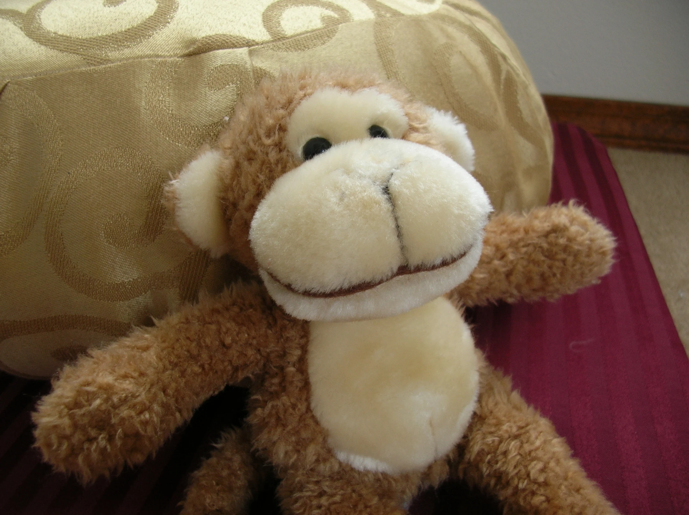 small brown stuffed monkey is posed in front of a gold background