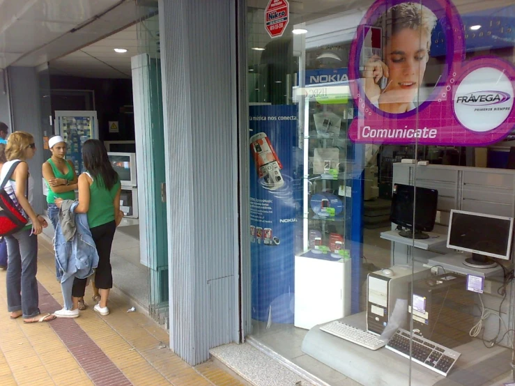 a group of people standing outside a store window with electronic equipment on display