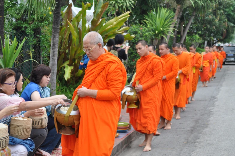 a line of monks in orange robes with bowls in each hand