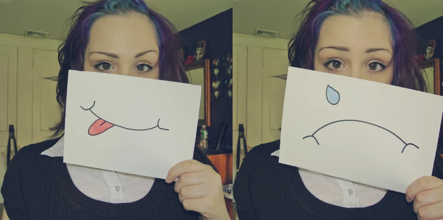 a woman holding a picture that shows her face drawn as a sad character
