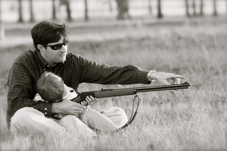 an adult holds a baby in the field while holding a gun