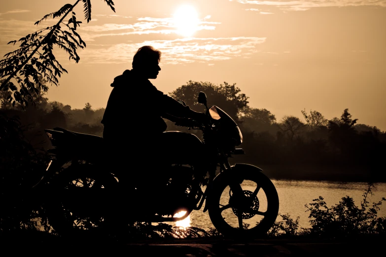 a man sits on a motorcycle next to the water