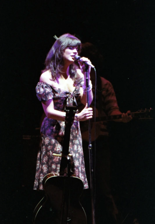 a woman in a purple floral dress standing by a microphone