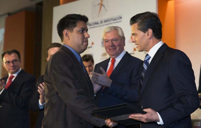 three men in suits standing in a room with a panel