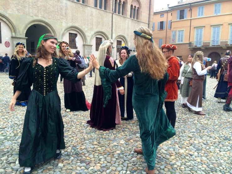 two women in medieval costumes stand in the middle of a cobblestone area while other women look on