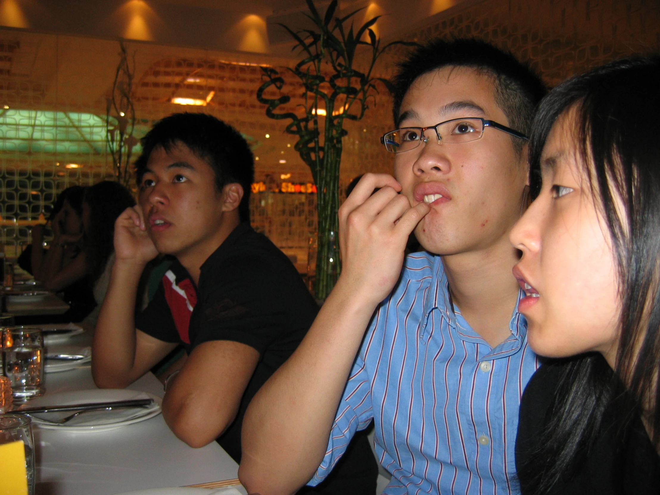 young man putting soing in his mouth sitting between people at table