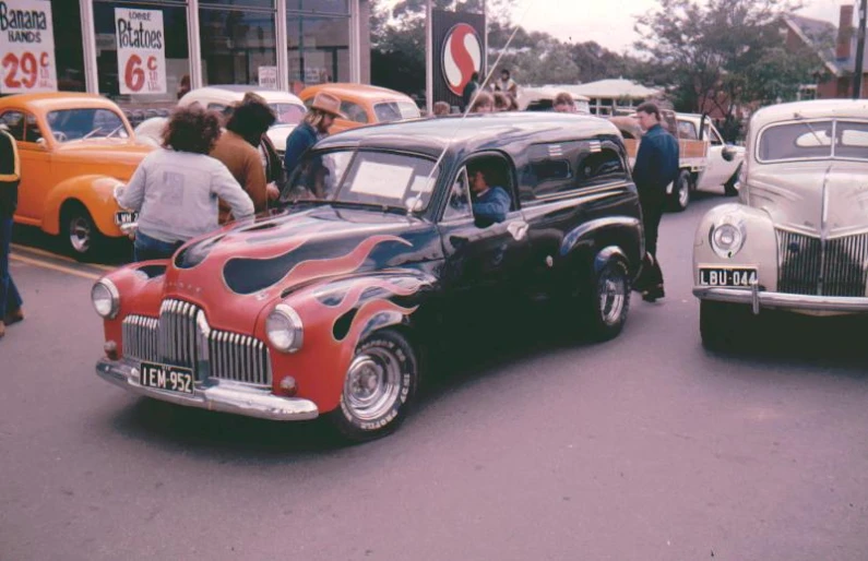 an old fashioned vehicle is parked on the street as people are waiting nearby