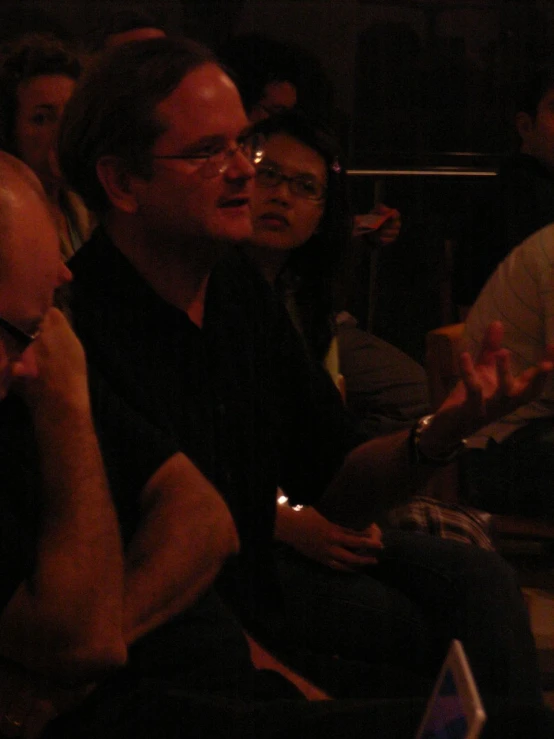 a man with glasses sitting on a chair with other people