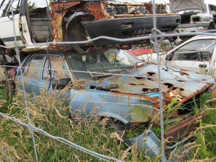 some old rusted cars behind a chain link fence
