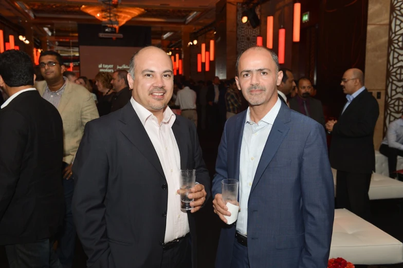 two men posing for the camera wearing suits and holding drinks