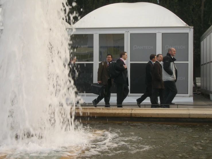two men walk by a large fountain with water coming out of it