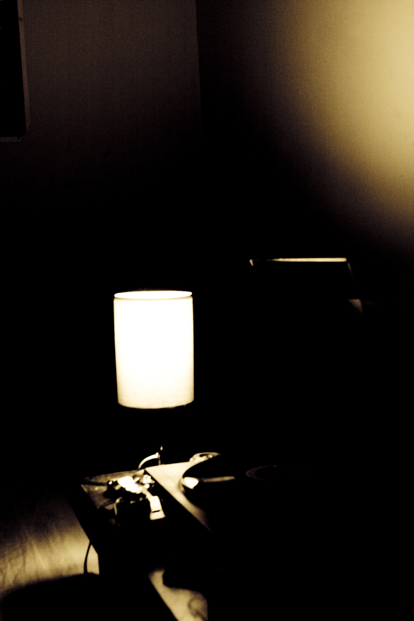 the corner of a dark room has a small desk with a lamp and papers