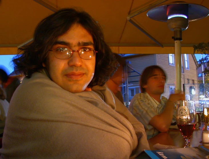 a man covered up sitting in a tent with two glasses