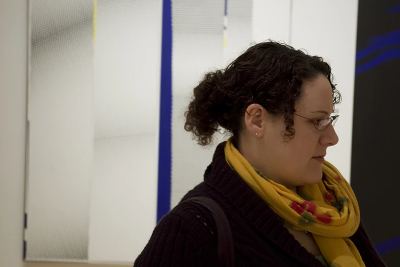 a woman in glasses stands in front of a painting