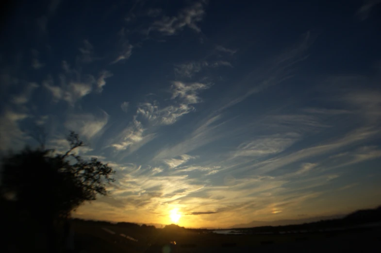 the sun sets behind some clouds and a tree