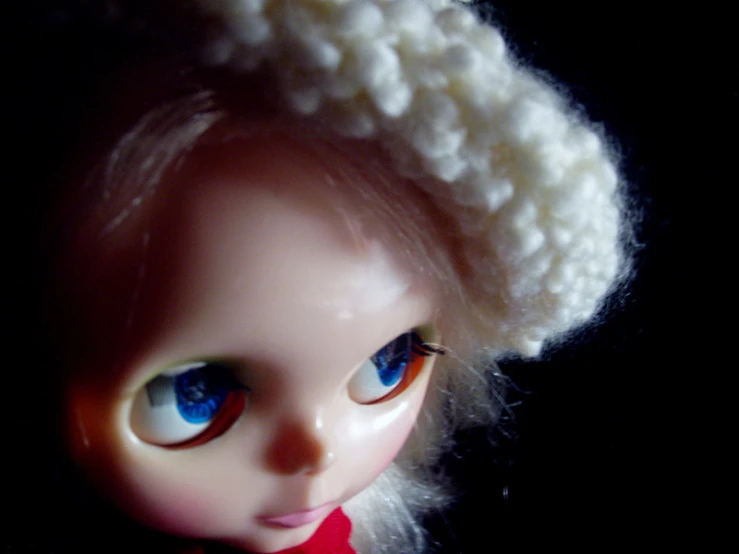 a doll with light blue eyes has a white head and a crocheted hat